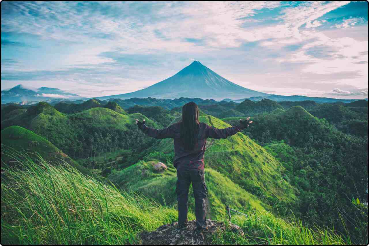 Person standing triumphantly on top of a grassy hill, arms outstretched to the sky